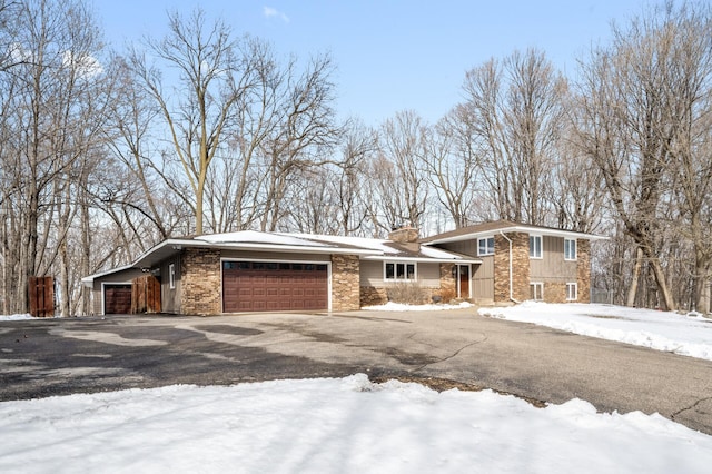 tri-level home with a garage, driveway, brick siding, and a chimney