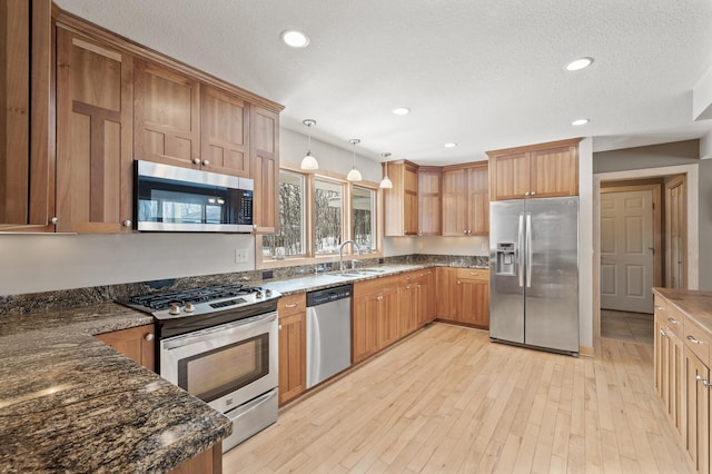 kitchen with light wood-type flooring, a sink, decorative light fixtures, a textured ceiling, and appliances with stainless steel finishes