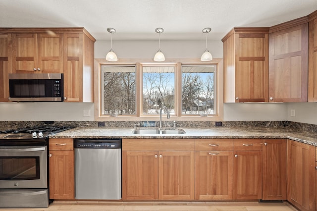 kitchen featuring a sink, stainless steel appliances, dark stone counters, and hanging light fixtures