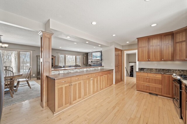 kitchen featuring ornate columns, an inviting chandelier, recessed lighting, stainless steel range, and light wood-style floors