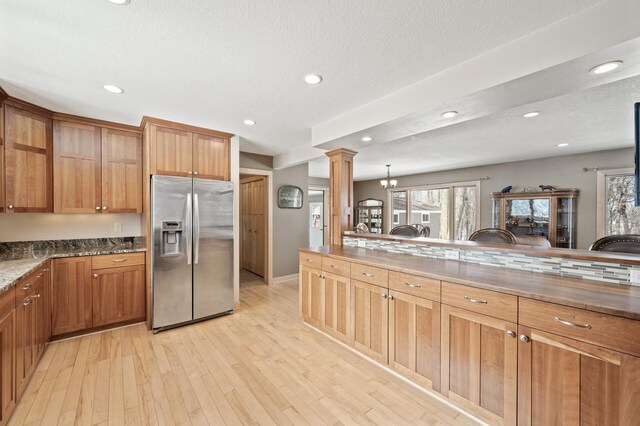 kitchen with stainless steel fridge with ice dispenser, dark stone counters, recessed lighting, light wood-style flooring, and ornate columns