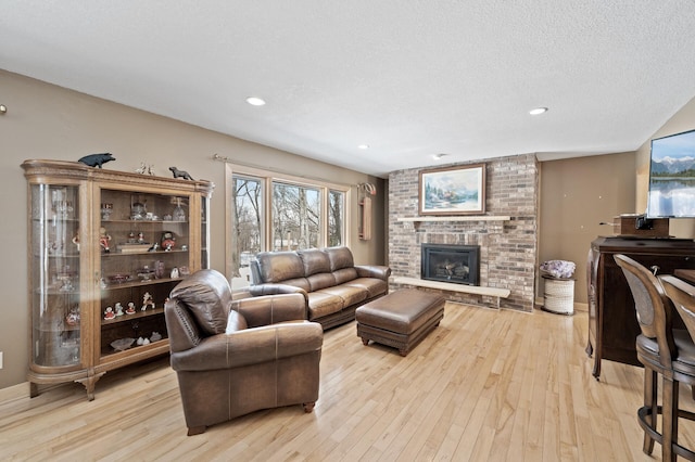 living area with a brick fireplace, baseboards, light wood finished floors, and a textured ceiling