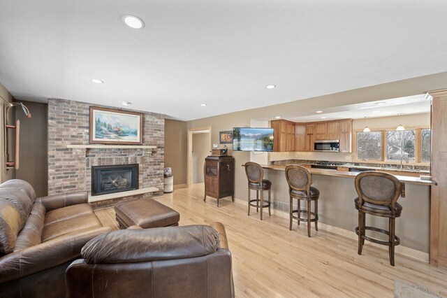 living room with light wood finished floors, recessed lighting, a brick fireplace, and baseboards