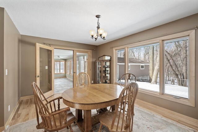 dining area featuring a notable chandelier, a textured ceiling, baseboards, and light wood-style floors