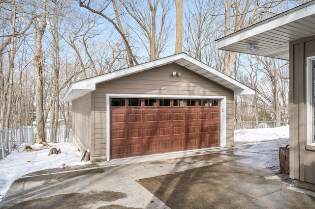 snow covered garage with a detached garage and fence