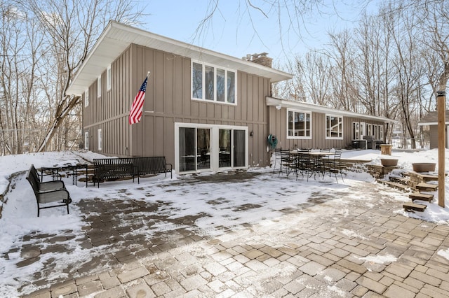 snow covered property with board and batten siding, a chimney, outdoor dining area, and a patio