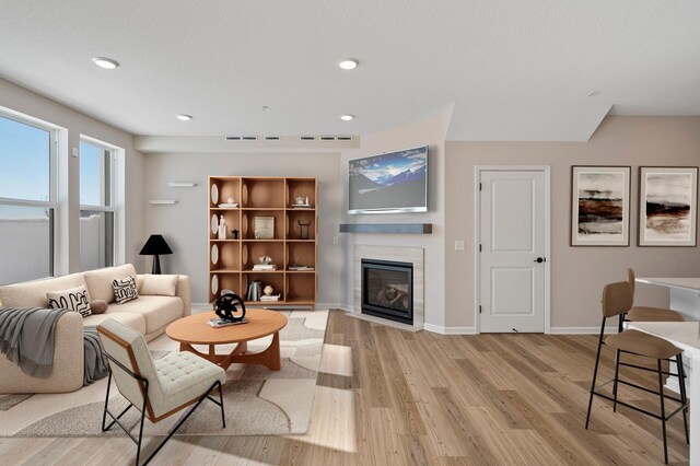 living area featuring a glass covered fireplace, baseboards, light wood-style flooring, and recessed lighting