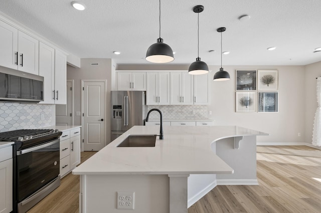 kitchen with a center island with sink, light wood-type flooring, stainless steel appliances, white cabinetry, and a sink