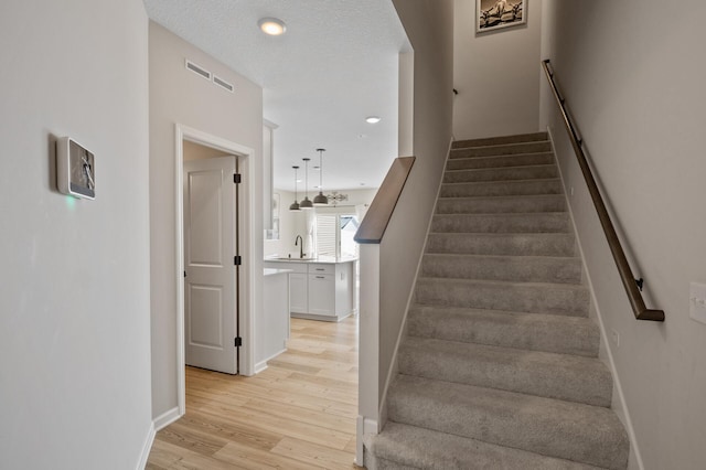 staircase featuring visible vents, wood finished floors, baseboards, and a textured ceiling