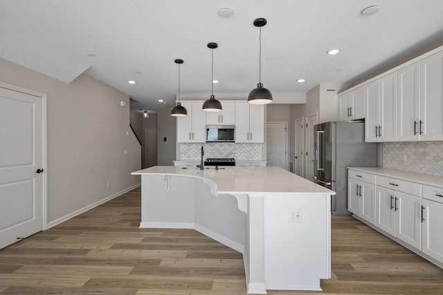 kitchen with light wood-type flooring, stainless steel appliances, a center island with sink, and white cabinetry