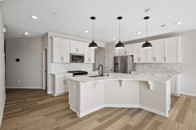 kitchen with a center island with sink, a sink, light wood-style floors, appliances with stainless steel finishes, and light countertops