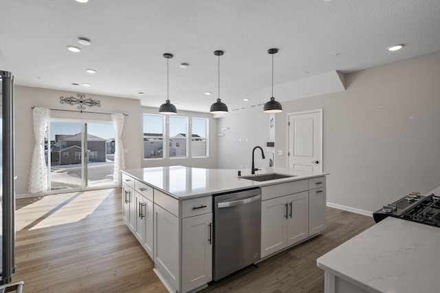 kitchen featuring a center island with sink, light wood-style flooring, a sink, pendant lighting, and dishwasher