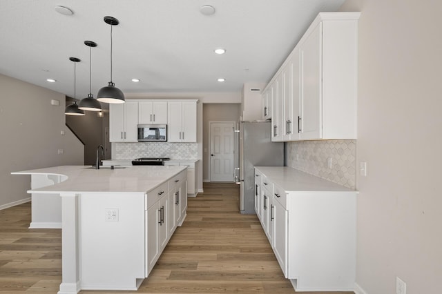 kitchen with an island with sink, light wood-style floors, appliances with stainless steel finishes, and a sink