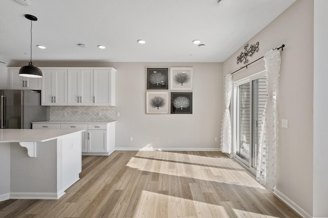 kitchen featuring white cabinetry, freestanding refrigerator, light wood finished floors, decorative backsplash, and light countertops