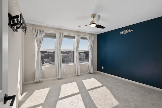 carpeted spare room featuring a ceiling fan and baseboards