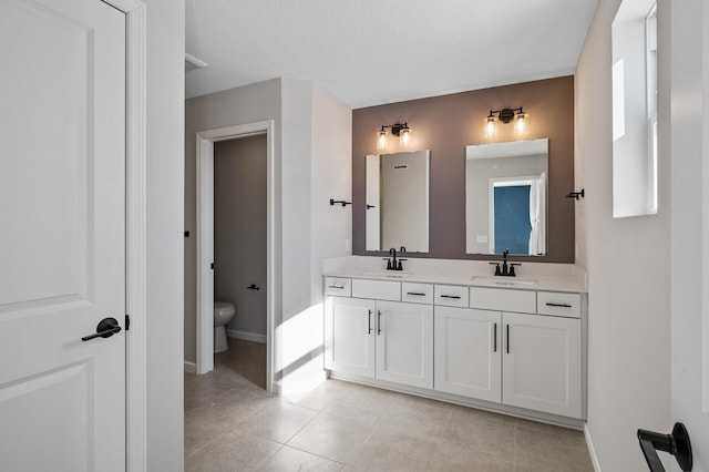 bathroom with double vanity, toilet, baseboards, and a sink