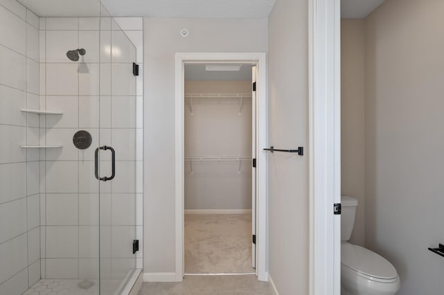 bathroom with a spacious closet, toilet, baseboards, and a stall shower