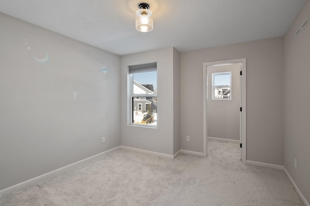 empty room featuring light carpet, visible vents, baseboards, and a textured ceiling