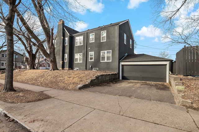 view of side of property featuring a detached garage, a chimney, and stucco siding