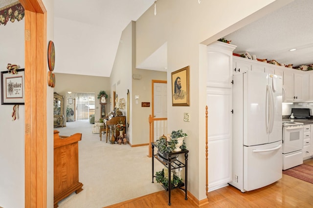 kitchen with baseboards, light colored carpet, vaulted ceiling, white appliances, and white cabinetry