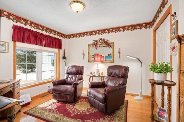 living area featuring baseboards, visible vents, a textured ceiling, and light wood-style floors