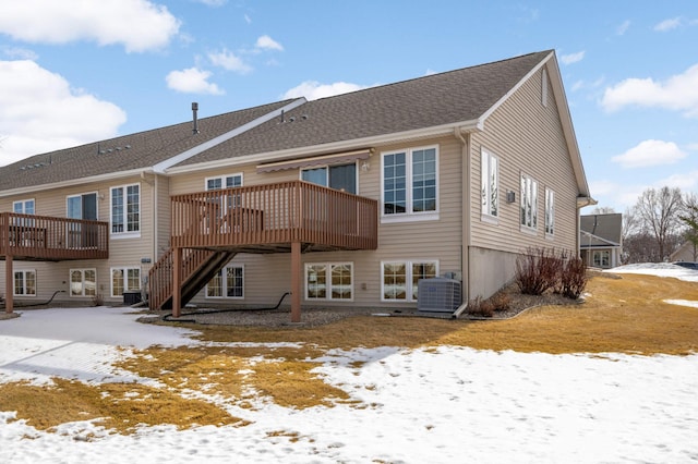 snow covered house with stairway, central AC unit, a deck, and a shingled roof