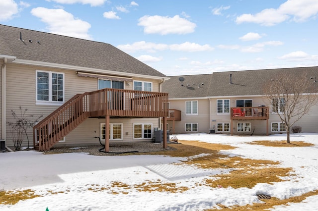 snow covered property featuring roof with shingles, central AC, and stairs