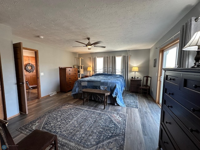 bedroom with ceiling fan, a textured ceiling, wood finished floors, visible vents, and baseboards