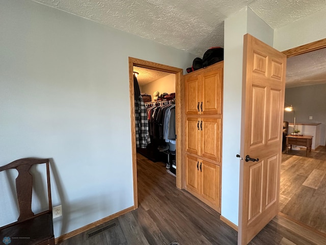 corridor with dark wood-style floors, a textured ceiling, visible vents, and baseboards