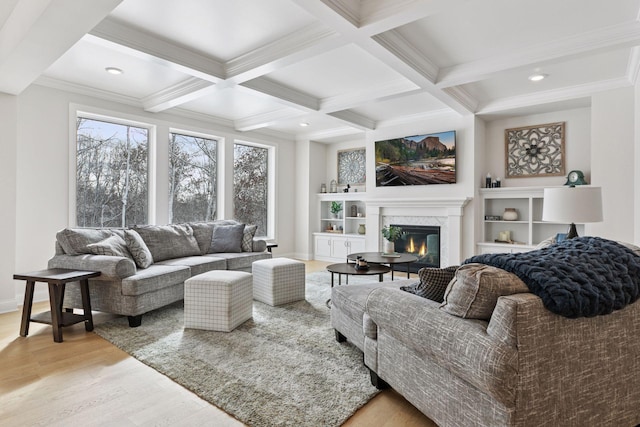 living area with light wood-type flooring, beam ceiling, ornamental molding, coffered ceiling, and a glass covered fireplace