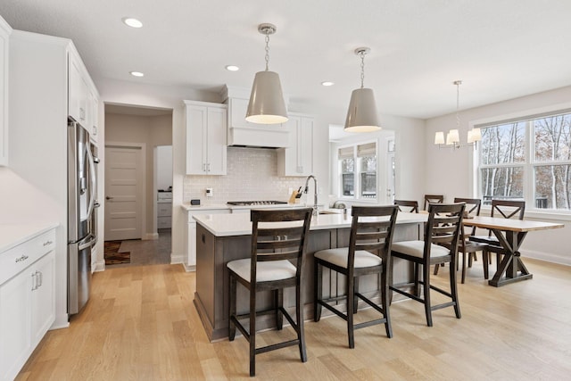 kitchen featuring tasteful backsplash, a breakfast bar area, light countertops, light wood-style flooring, and stainless steel fridge