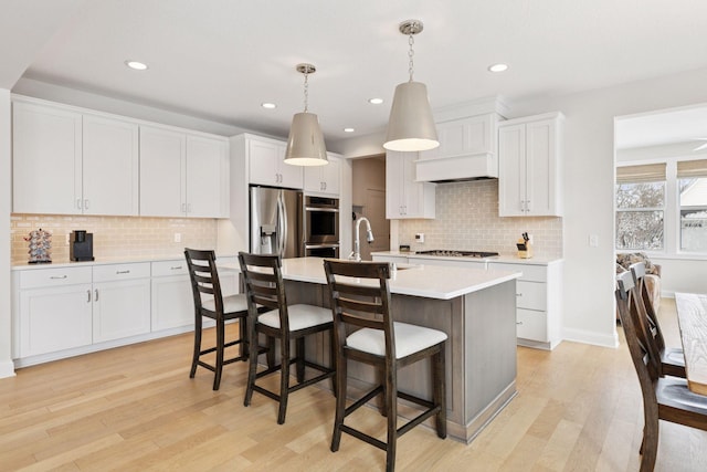 kitchen featuring a center island with sink, white cabinetry, light wood-style floors, appliances with stainless steel finishes, and light countertops