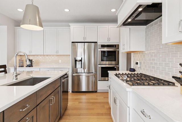 kitchen featuring a sink, wall chimney range hood, white cabinets, and stainless steel appliances