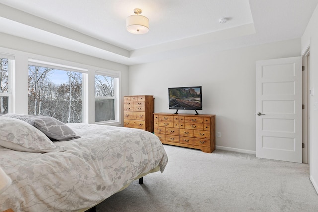 carpeted bedroom with a raised ceiling and baseboards