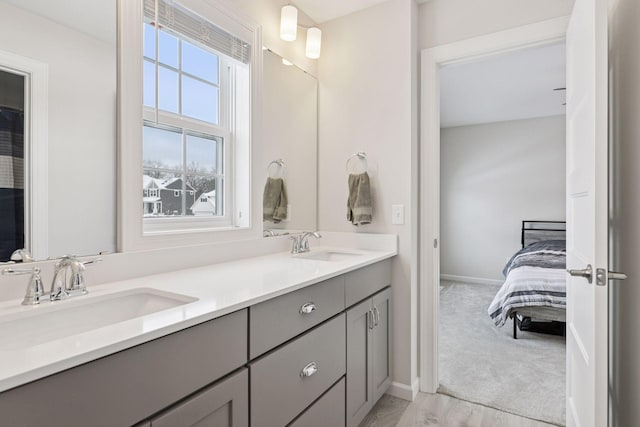 bathroom with double vanity, ensuite bathroom, baseboards, and a sink