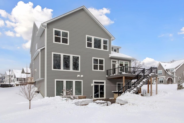 snow covered house with a deck, stairway, and french doors