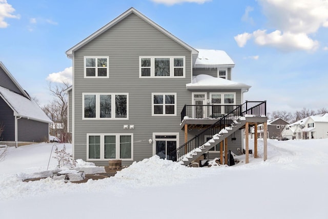 snow covered house with stairway and a wooden deck