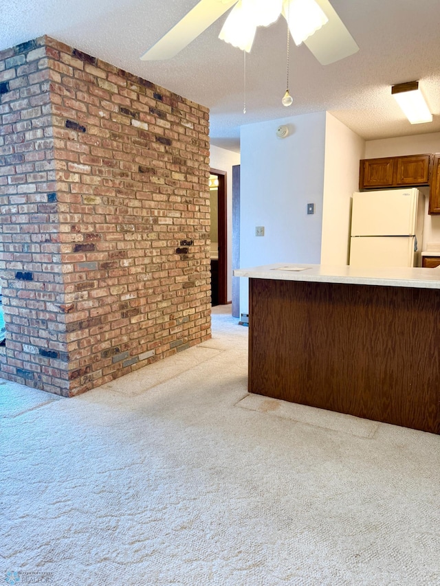 kitchen with light countertops, light colored carpet, freestanding refrigerator, a textured ceiling, and brick wall