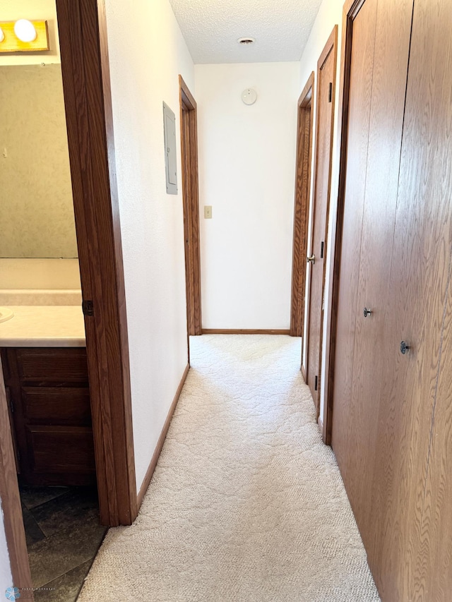 hall featuring electric panel, light colored carpet, a textured ceiling, and baseboards