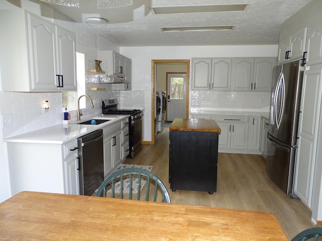 kitchen featuring light wood finished floors, washing machine and clothes dryer, appliances with stainless steel finishes, a sink, and a kitchen island