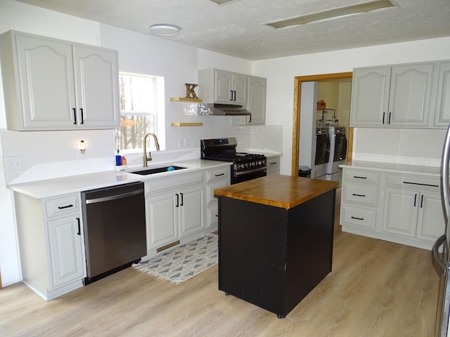 kitchen featuring stainless steel appliances, a sink, wood counters, light wood-type flooring, and washer and dryer