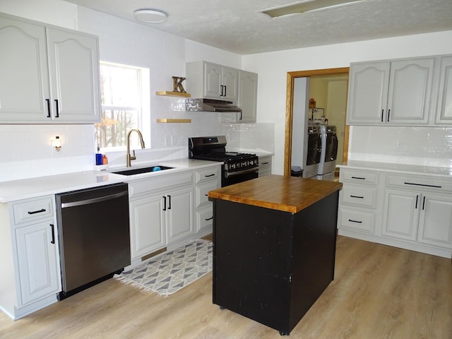 kitchen with butcher block counters, a sink, appliances with stainless steel finishes, independent washer and dryer, and light wood finished floors