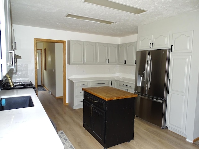 kitchen with light wood-style flooring, stainless steel refrigerator with ice dispenser, wooden counters, and a center island