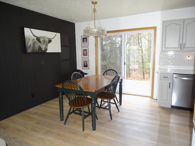 dining space featuring light wood-type flooring, wood walls, and a notable chandelier