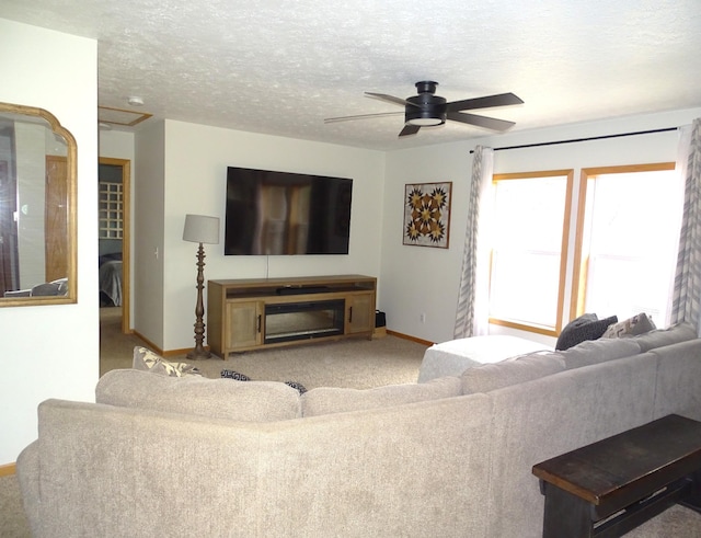 living area featuring carpet, baseboards, ceiling fan, and a textured ceiling