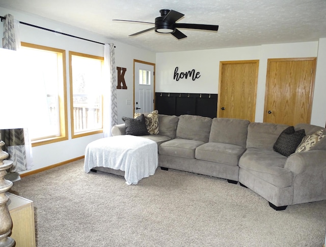 carpeted living area with a textured ceiling, ceiling fan, baseboards, and a healthy amount of sunlight