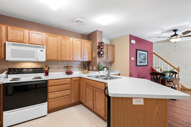 kitchen featuring white microwave, a peninsula, range with electric cooktop, a sink, and light countertops