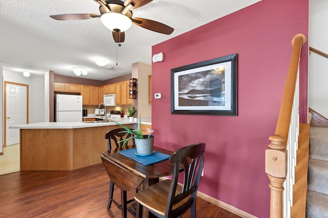 dining room featuring ceiling fan, a textured ceiling, wood finished floors, baseboards, and stairs