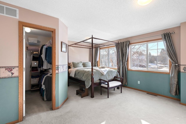 carpeted bedroom with a walk in closet, a closet, visible vents, a textured ceiling, and baseboards