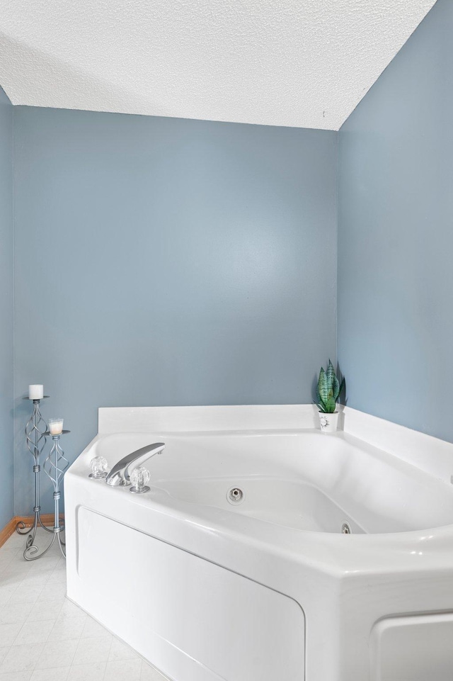 full bath with a textured ceiling, a tub with jets, and baseboards